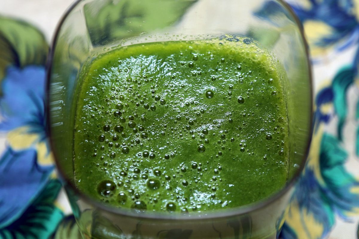 A green smoothie in a glass beside its blended ingredients.
