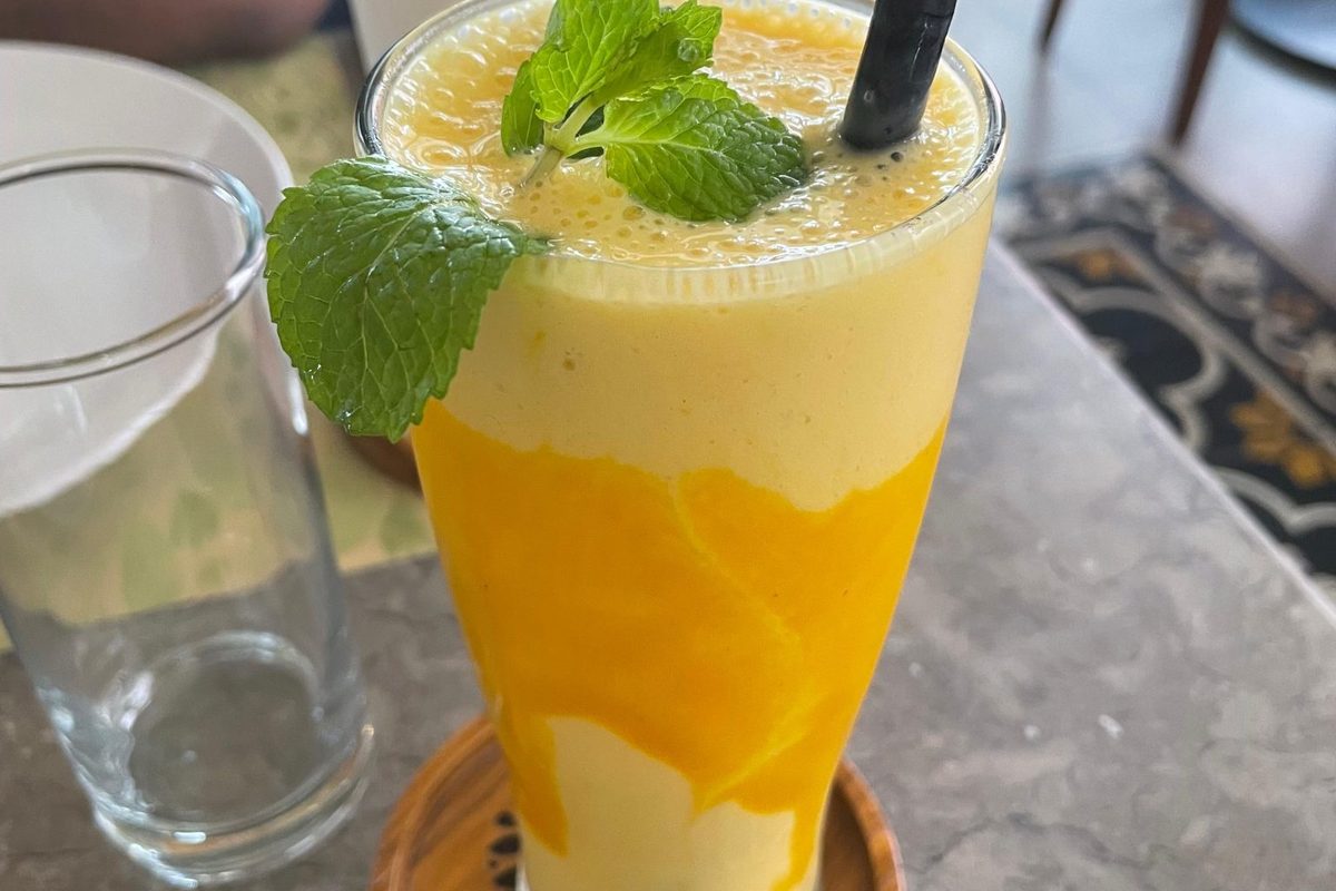 A bright fruit smoothie in a tall glass on a kitchen counter.