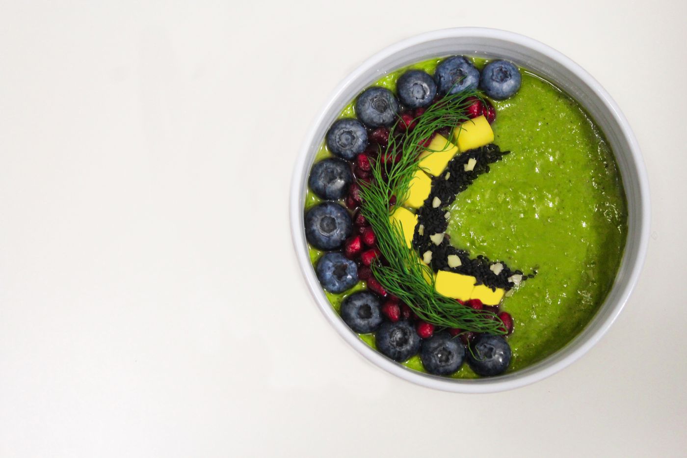 A green smoothie in a glass beside its blended ingredients.